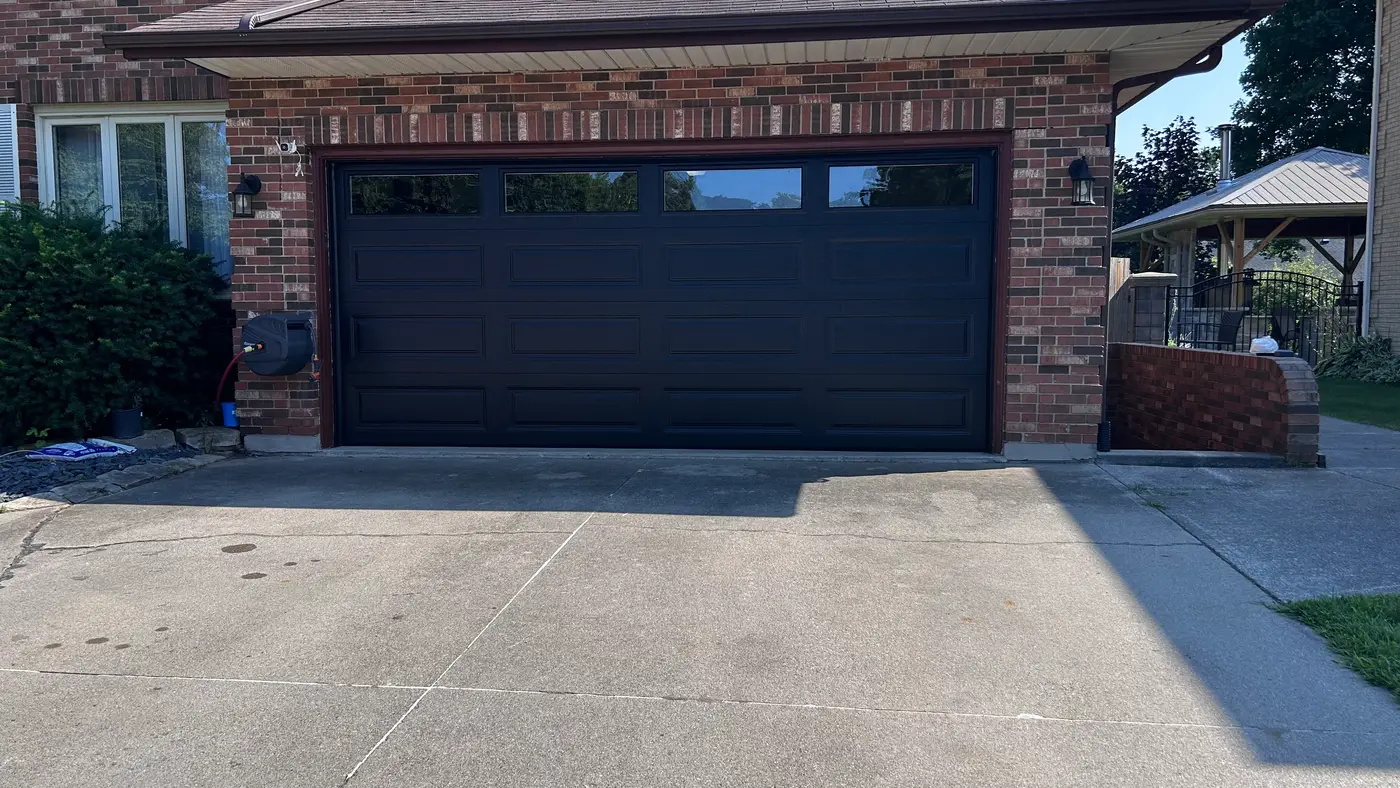 A modern garage door with tinted horizontal glass panels reflecting the sky at dusk