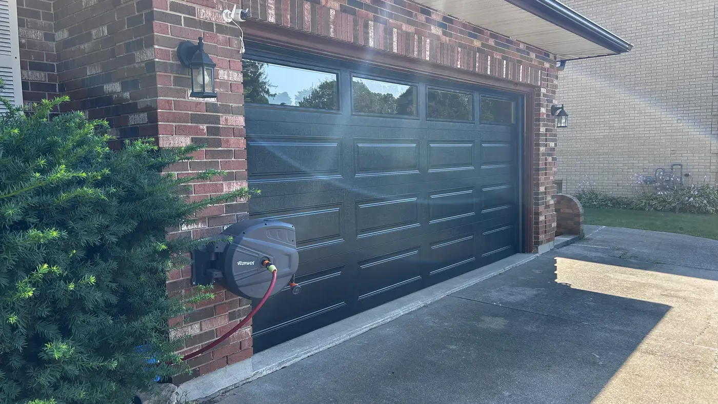 Angled view of a new black raised-panel garage door installed on a brick home in Ingersoll, ON