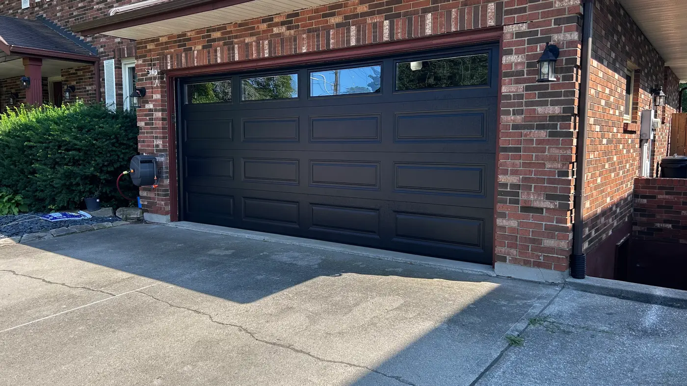 A newly installed dark garage door on a suburban brick home