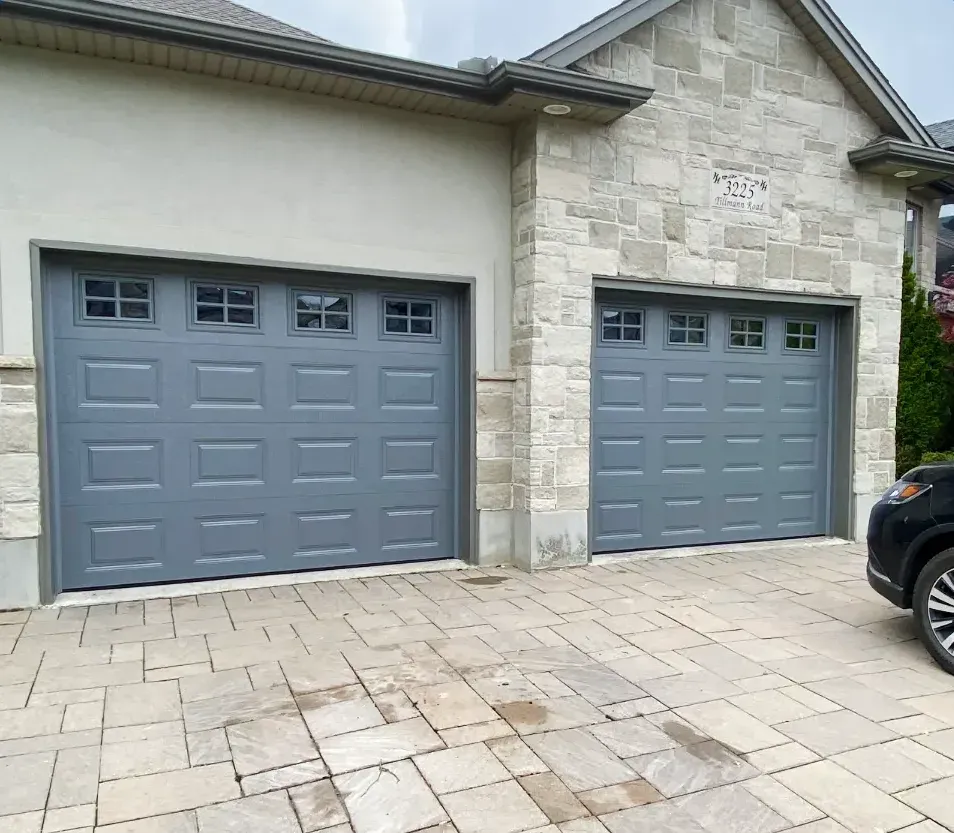 Two grey raised-panel garage doors with windows installed on a stone home in Masonville, London